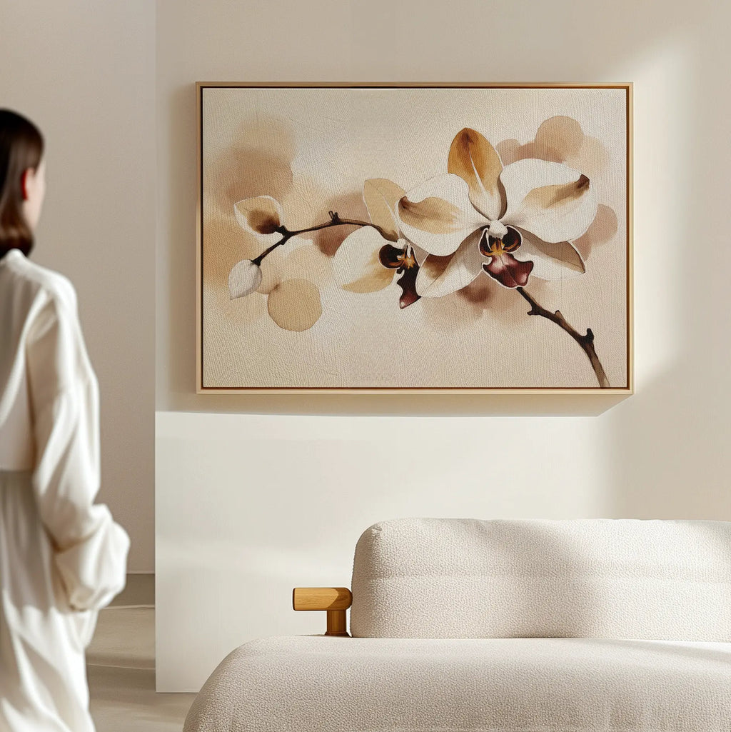 A woman in a white robe stands in a minimal, neutral-toned room, admiring the Vanilla Bloom Canvas Art—a large framed orchid print—hanging above a light-colored sofa.