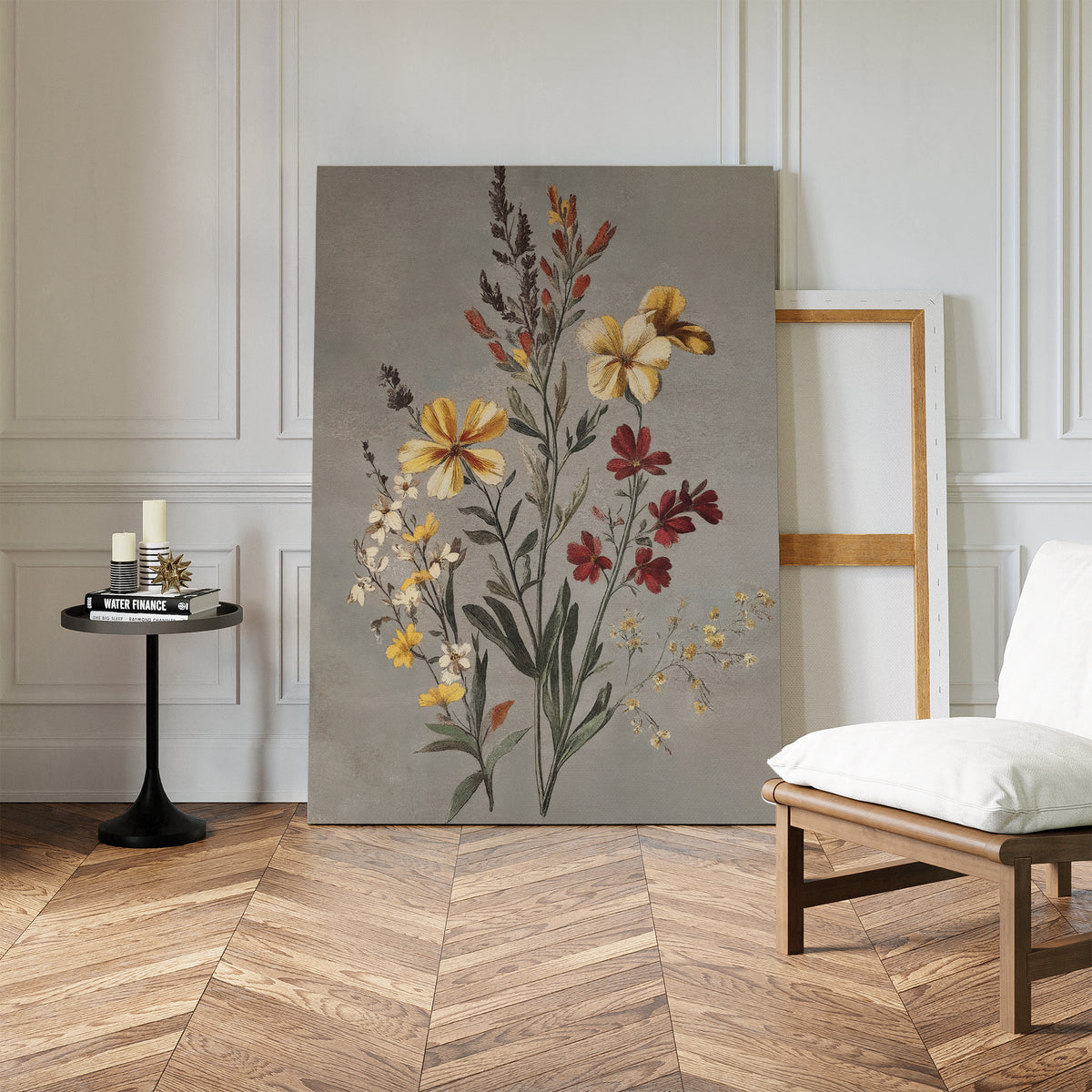 The Velvet Petals Canvas Art leans against a white paneled wall near an empty frame. A black round table with candles and books sits nearby, and a white cushioned chair is placed on the herringbone wood floor.