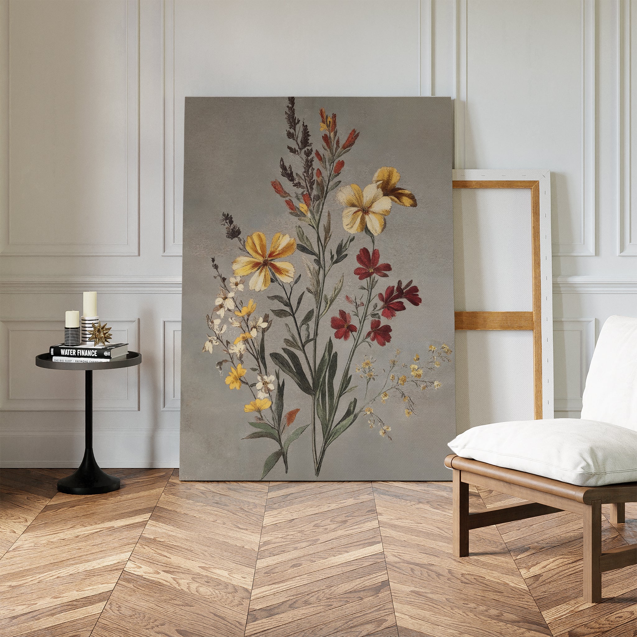 The Velvet Petals Canvas Art leans against a white paneled wall near an empty frame. A black round table with candles and books sits nearby, and a white cushioned chair is placed on the herringbone wood floor.