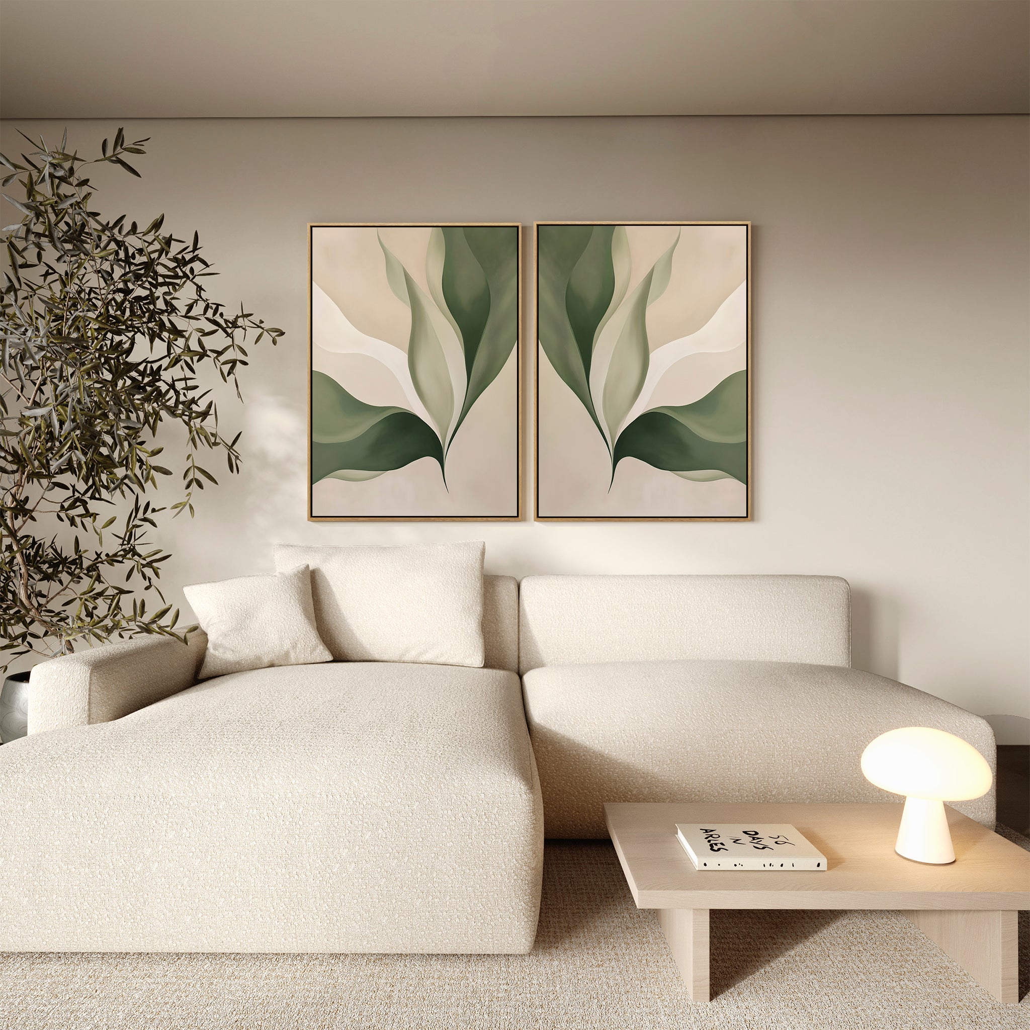 A modern living room with a cream textured sectional sofa, Verdant Grace Set of 2 minimalist wall art featuring green and beige leaf prints, a small wooden coffee table with a round lamp, and a plant in the corner.