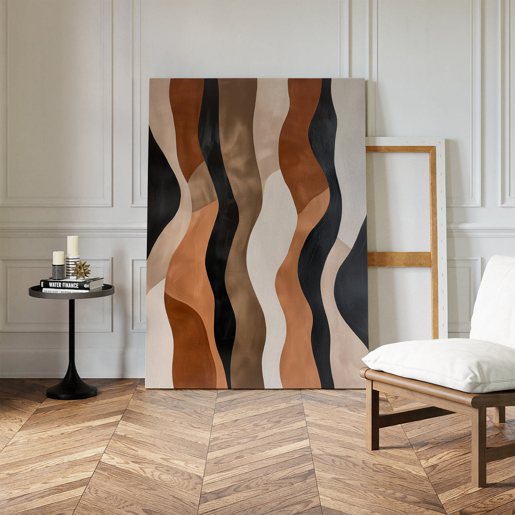 The Wavy Patterns Abstract Canvas Art, featuring black, brown, tan, and beige lines, leans against a white paneled wall in a stylish room with herringbone wood floors, a modern side table with candles, and a contemporary white chair.