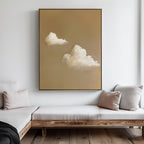 A minimalist living room features a wooden-framed couch with beige and gray cushions, complemented by the Whispering Clouds wall art—an elegant painting of two fluffy white clouds on a tan background—that enhances the decor.