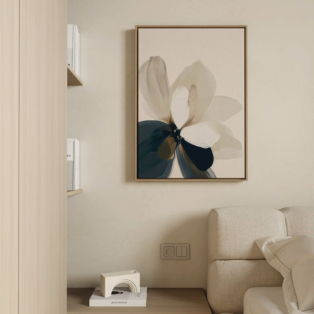 A minimalist living room corner features a beige sofa, the Whispering Petals Canvas Art - Vertical with an abstract flower design, and shelves with white books and a small decorative object for a serene, neutral atmosphere.