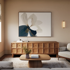 A modern living room with light walls, a wooden sideboard, the Whispering Petals Canvas Art - Horizontal, a round coffee table with a vase, beige sofa, rug, and wall sconce—perfect for elevating your living room decor.