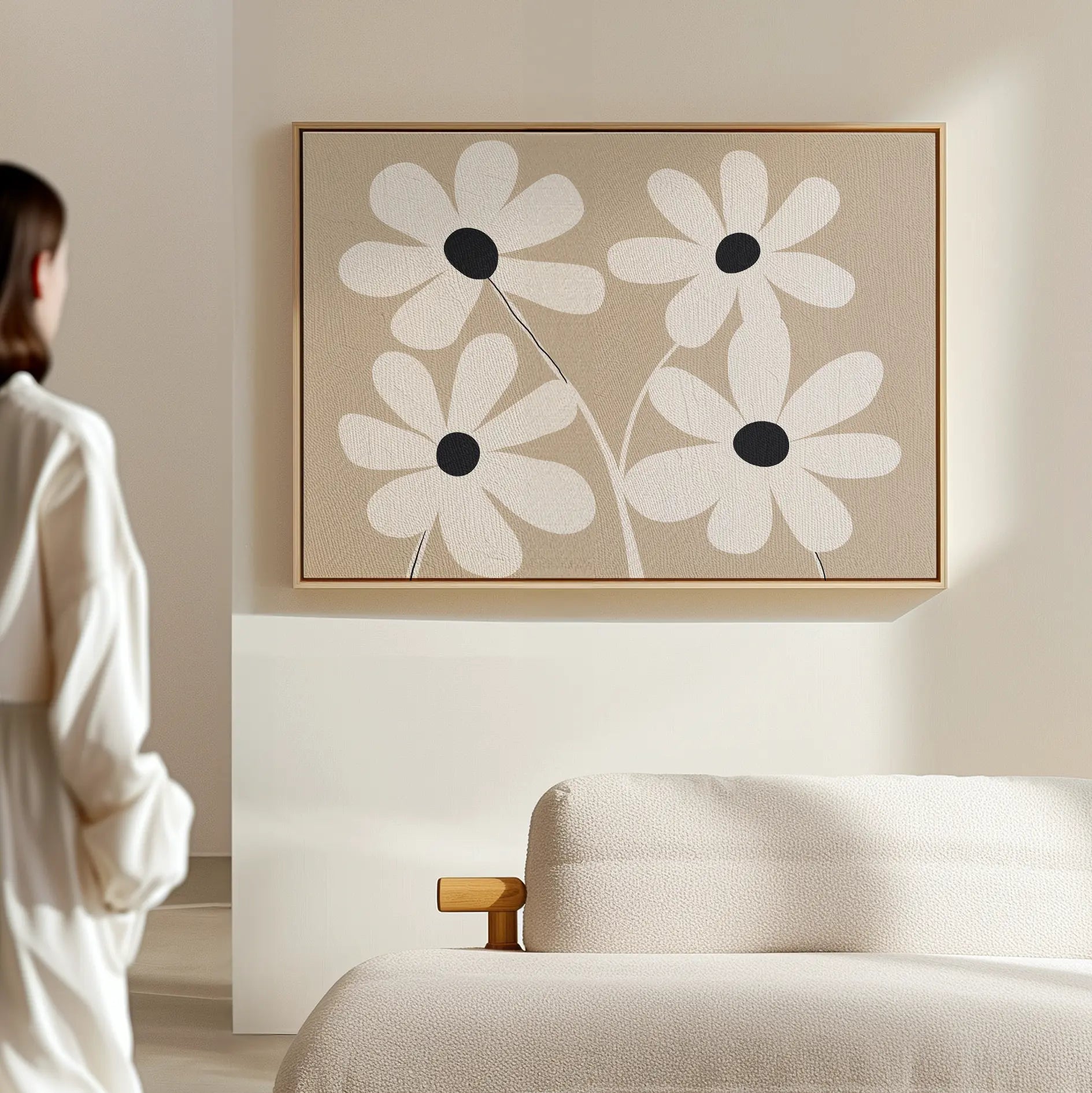 A person stands in a minimal, light-filled room with a beige couch and the White Blooms Canvas Art—an abstract print of white flowers with black centers—displayed on the wall.