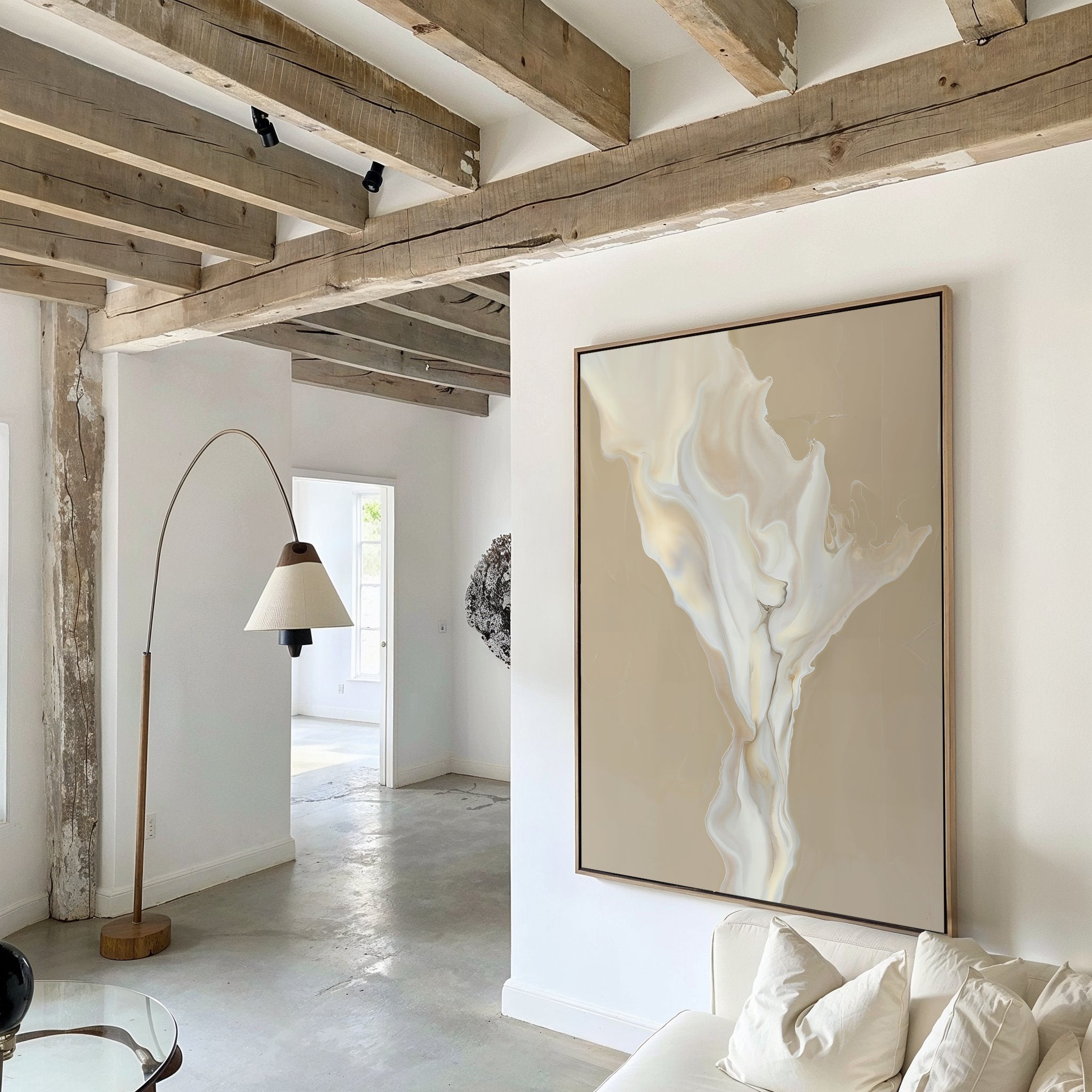 A minimalist living room with exposed wooden beams, a white sofa, and a curved floor lamp features White Flame Abstract Canvas Art on a white wall, elevating the decor as natural light streams in from an adjacent room.