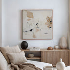 A cozy, neutral-toned living room with a beige sofa, soft pillows, wooden sideboard, vases, and minimalist wall art—a framed White Whispers Canvas Art in cream and tan tones—perfectly completes the decor.