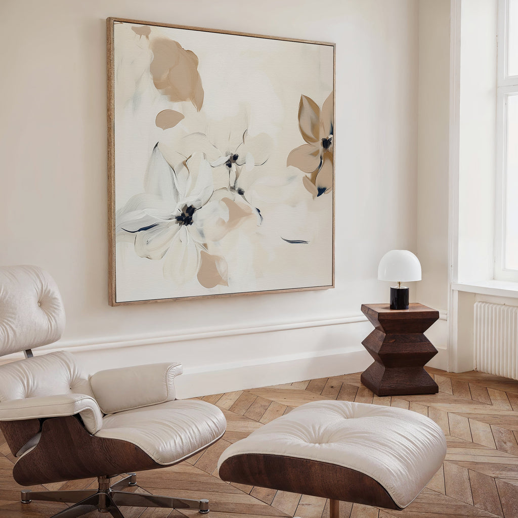 A modern living room with a white leather lounge chair and ottoman, wooden side table with a white lamp, and the striking White Whispers Canvas Art. Light walls and herringbone wood flooring complete the stylish decor.