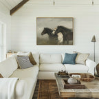 A cozy living room with a white sectional sofa, assorted throw pillows, a rustic wooden coffee table, and the Wild Current Canvas Art above the couch. The decor features neutral tones and natural textures.