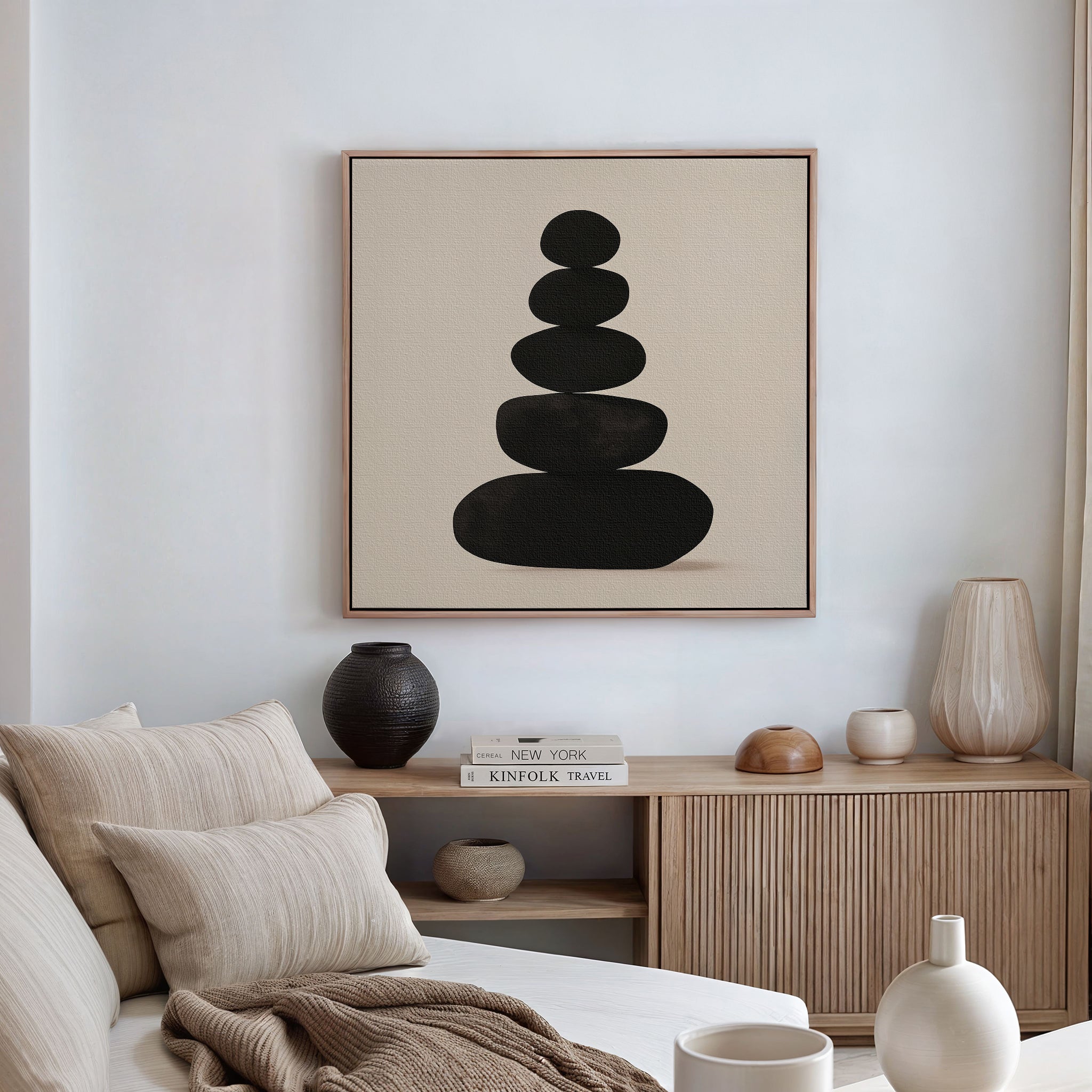 A minimal, modern living room with a beige sofa, neutral cushions, a wooden sideboard adorned with decor items, and calming living room decor featuring the Zen Balance Canvas Art—a large framed artwork of stacked black stones.