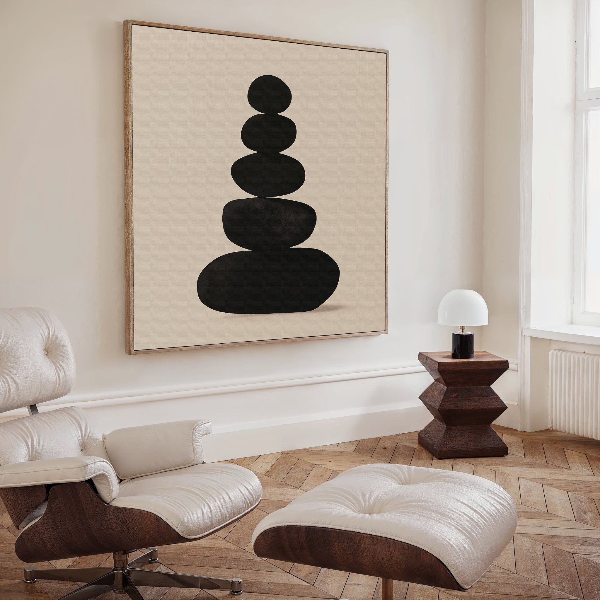 A modern living room with a white lounge chair and ottoman, a wooden side table with a white lamp, and the Zen Balance Canvas Art—a large minimalist print with stacked black shapes—perfect for stylish living room decor.