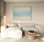 A modern living room featuring a light beige sectional, wooden coffee table, minimalist black bowl, tall plant, and the Airy Shore Canvas Art - Horizontal for a calm seaside vibe. Neutral tones and soft natural light complete the look.