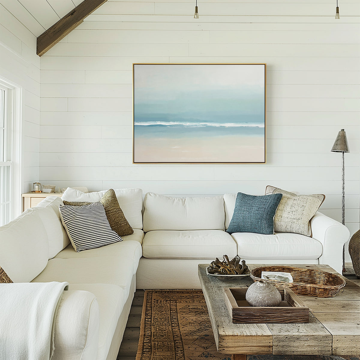 A bright, airy living room with white shiplap walls, a large white sectional topped with throw pillows, a rustic wood coffee table, and the Airy Shore Canvas Art - Horizontal above the sofa enhancing the serene seaside vibe.