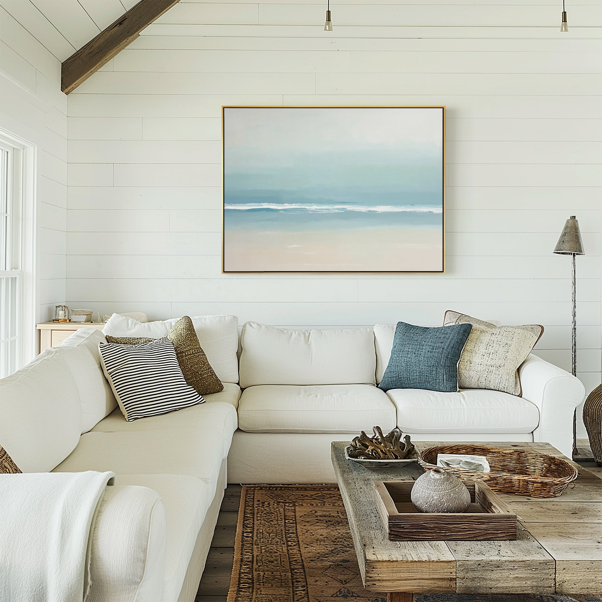 A bright, airy living room with white shiplap walls, a large white sectional topped with throw pillows, a rustic wood coffee table, and the Airy Shore Canvas Art - Horizontal above the sofa enhancing the serene seaside vibe.