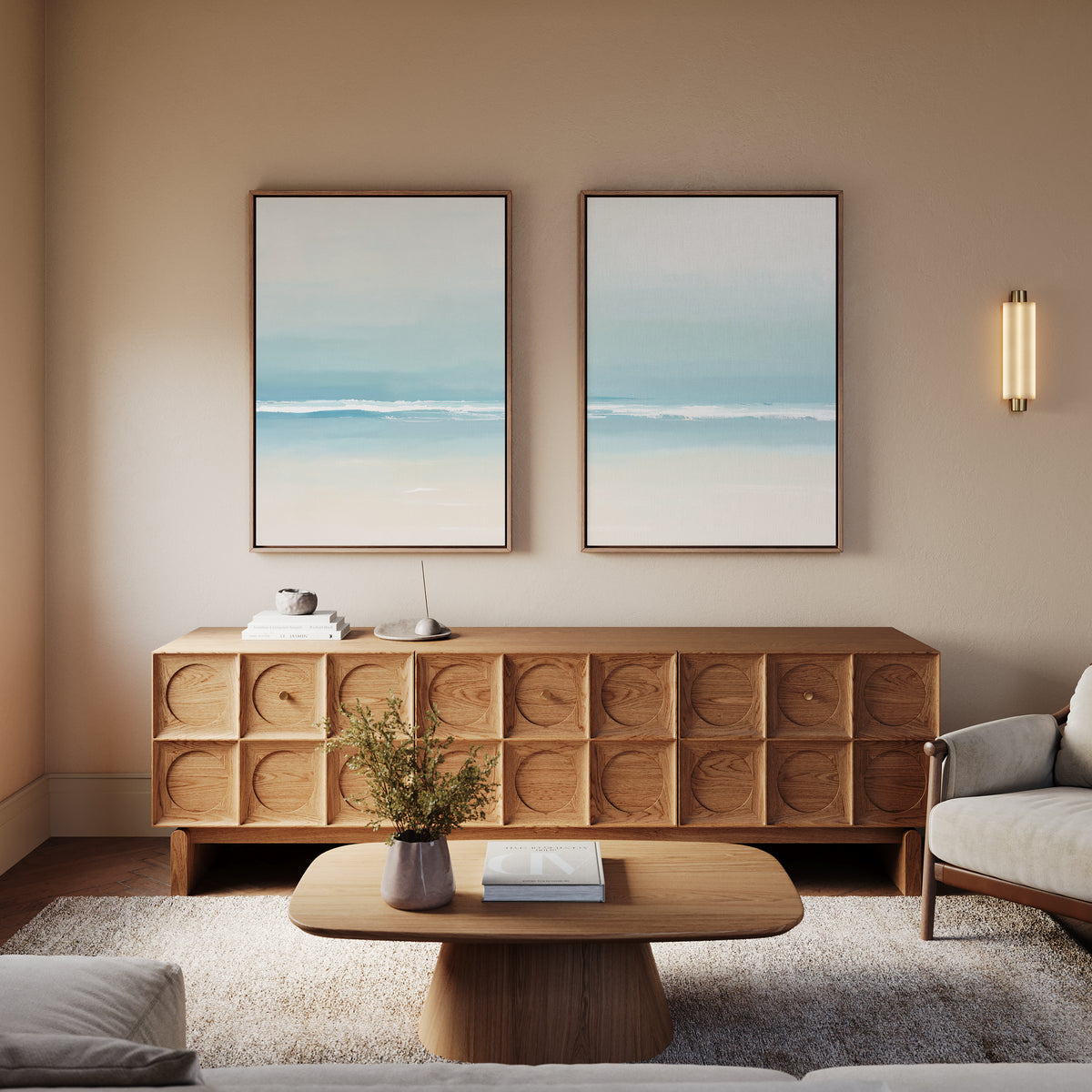 A modern living room with a wooden coffee table, a light wood sideboard with geometric patterns, the Airy Shore - Set Of 2 wall art prints, a small plant, and a light-colored armchair. Soft neutrals create a calm atmosphere.