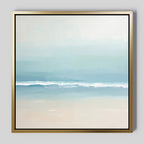 The Airy Shore Canvas Art - Square is a minimalist coastal print depicting a serene seascape with gentle waves and soft blue, white, and beige hues, elegantly framed in a slim metallic gold frame.