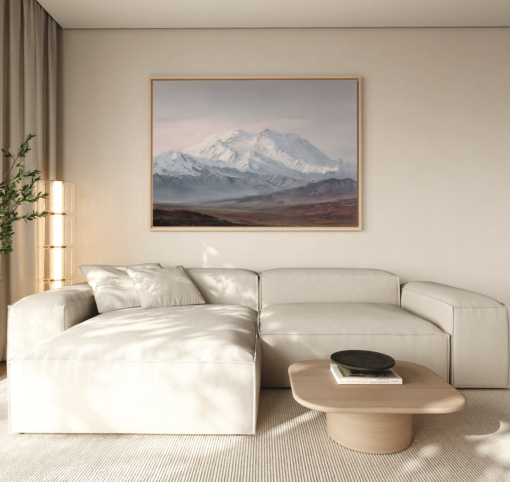 A modern living room features a light beige sectional sofa, a wooden coffee table, and the Alpine Majesty Canvas Art - Horizontal above the sofa. Soft natural light streams in through a window with sheer curtains.