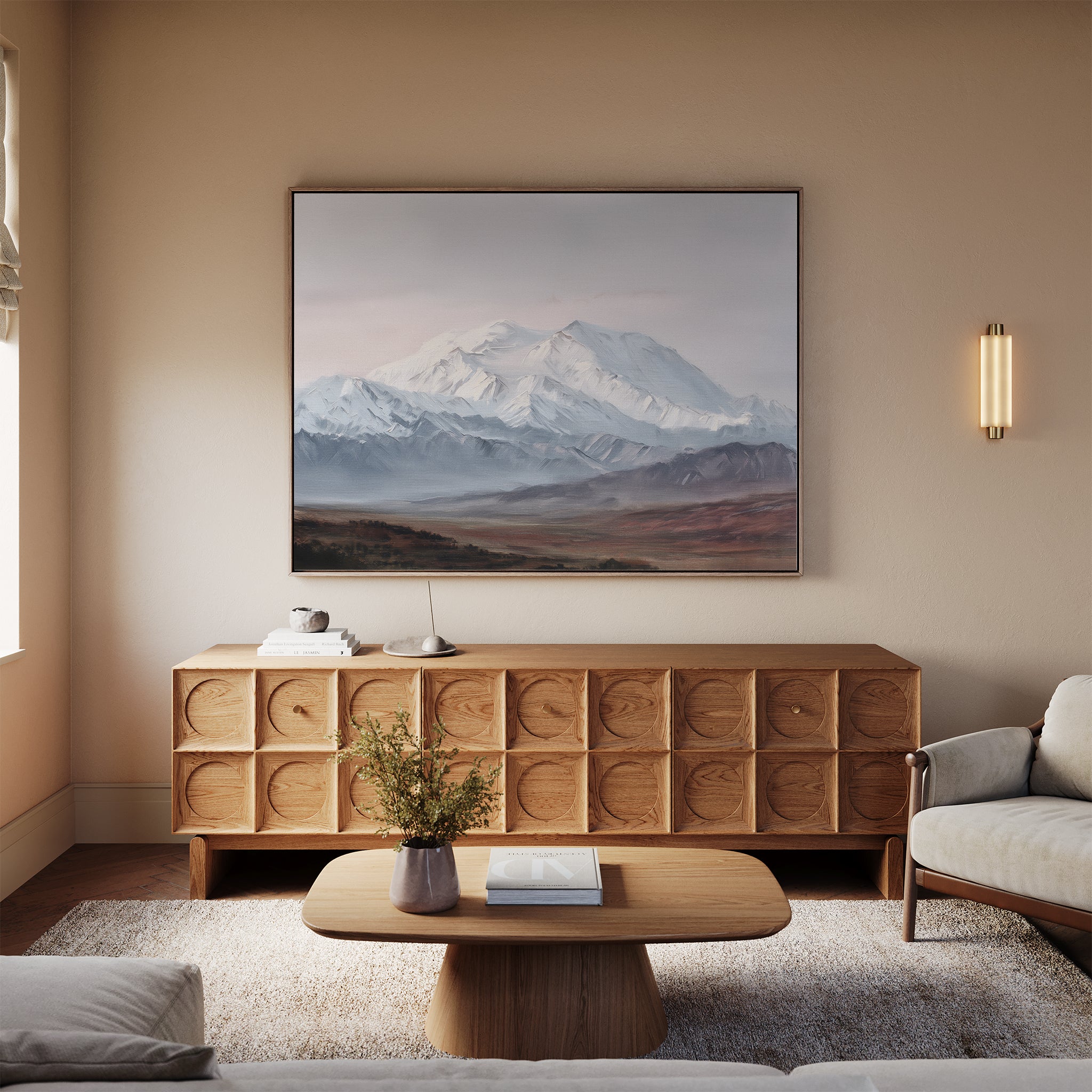 A cozy living room with a modern wood sideboard, low coffee table, and light-colored sofa features the Alpine Majesty Canvas Art - Horizontal, showcasing a balanced mountain palette. A small vase with flowers and books sit on the table.