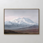 The Alpine Majesty Canvas Art - Horizontal features snow-covered mountain peaks beneath a cloudy sky, with muted green-brown hills in front, creating a serene focal point on any plain white wall.