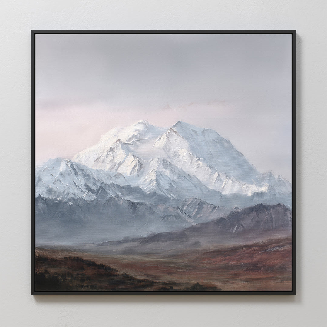 The Alpine Majesty Canvas Art - Square features a framed print of a snow-capped mountain under cloudy skies, with rocky foothills and a brown plain in front, displayed on a light wall.