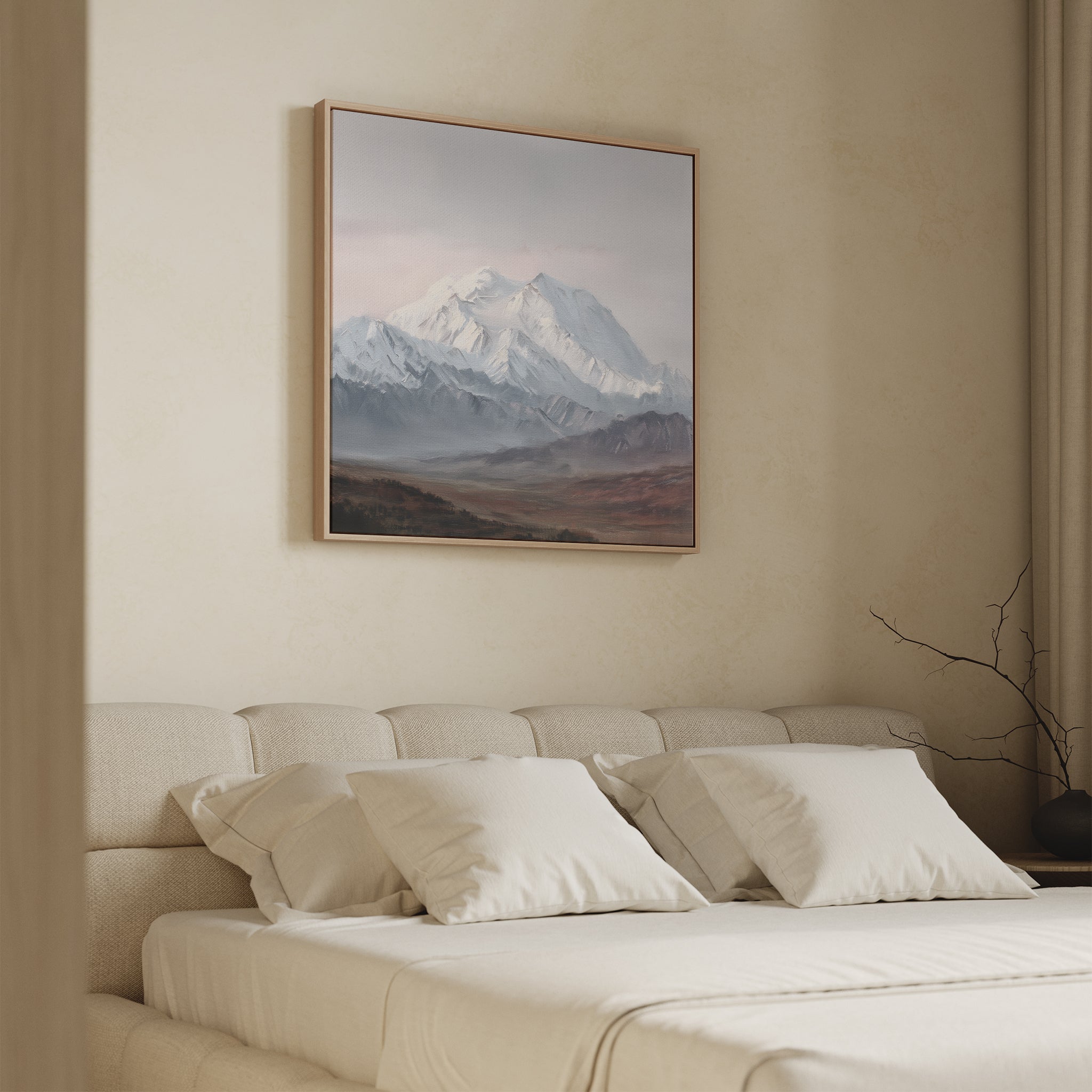 A bedroom features a beige bed with white pillows and a neutral comforter. Above the bed hangs the Alpine Majesty Canvas Art - Square, while a bare branch in a vase decorates the nightstand on the right.