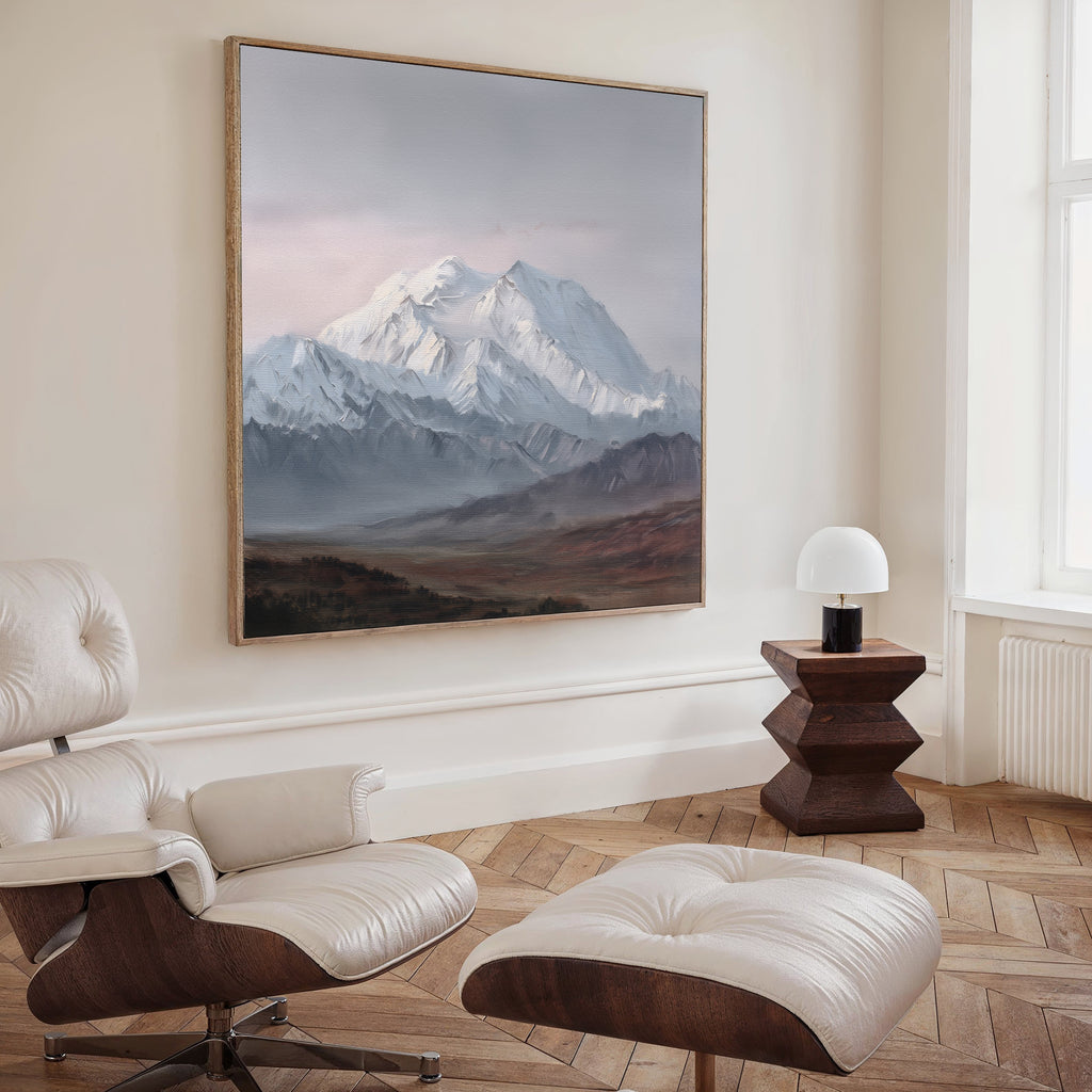 A modern living room features a leather lounge chair with ottoman, a small wooden side table with a white lamp, and the Alpine Majesty Canvas Art - Square displayed prominently on the wall.