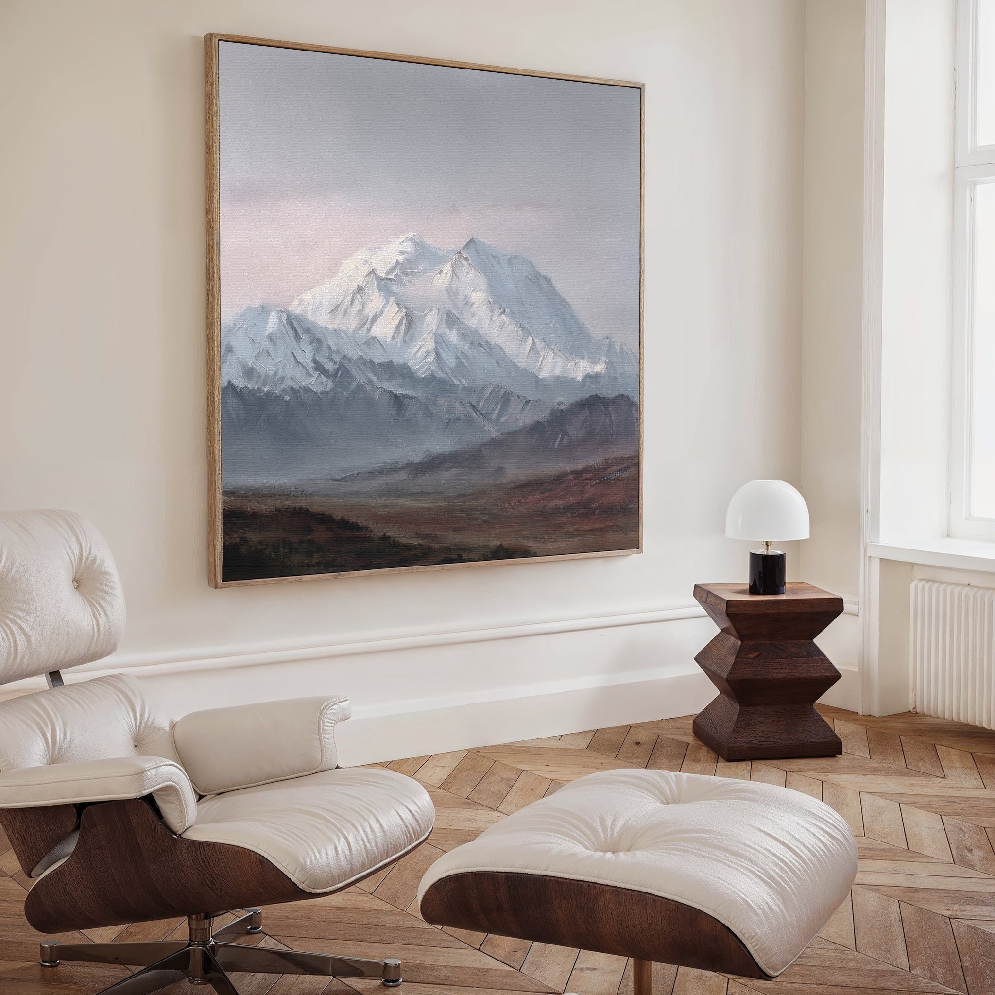 A modern living room features a leather lounge chair with ottoman, a small wooden side table with a white lamp, and the Alpine Majesty Canvas Art - Square displayed prominently on the wall.