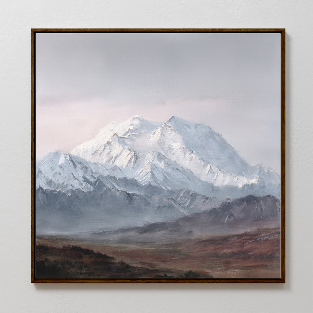 The Alpine Majesty Canvas Art - Square showcases a snow-capped mountain range under a cloudy sky, rugged foothills, and brown foreground terrain, beautifully displayed on a plain white wall.