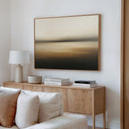 A modern living room with a beige sofa, wooden sideboard, white lamp, stacked books, and the Amber Fields Canvas Art - Horizontal featuring neutral and amber tones hanging on the wall.