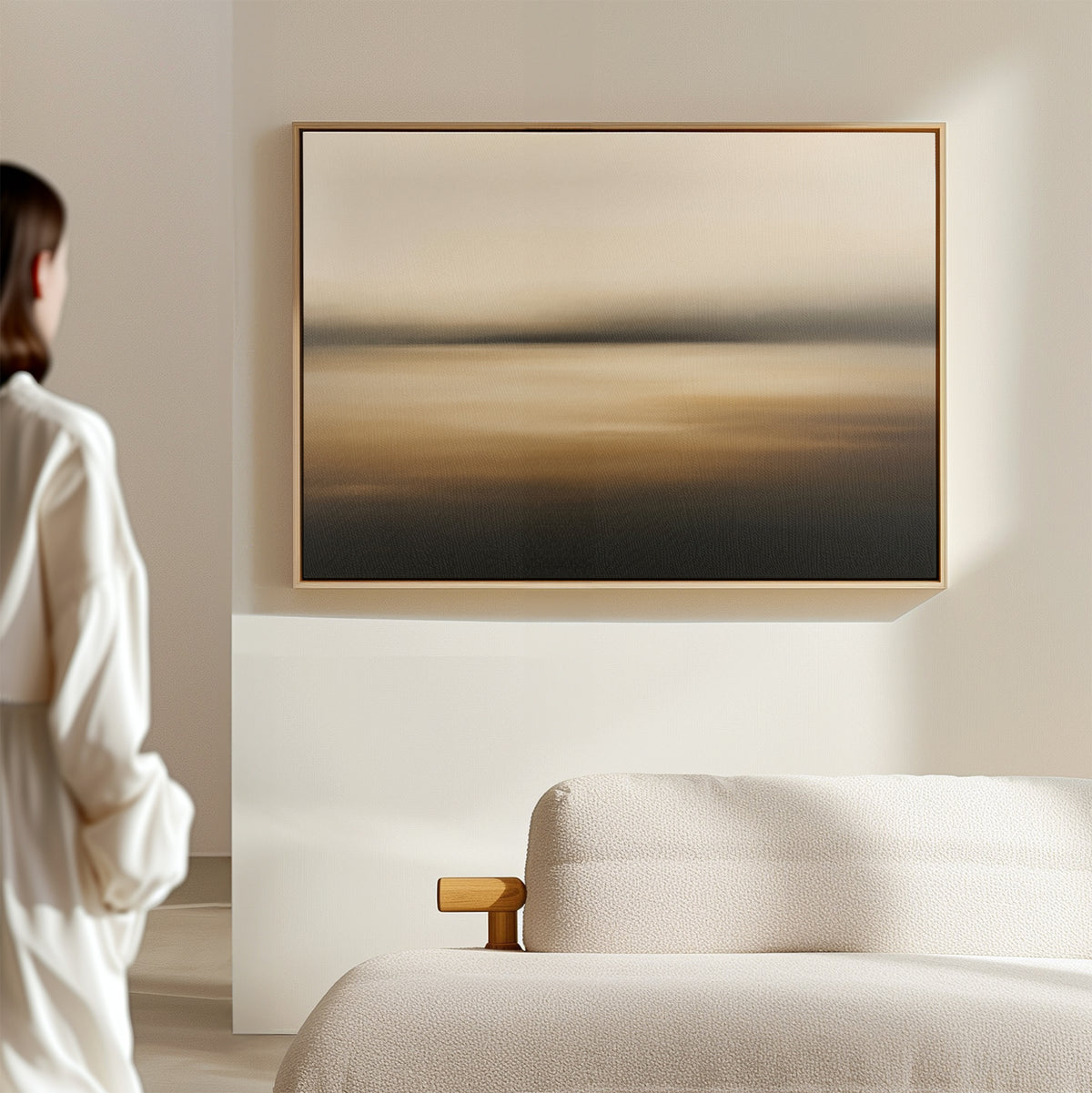 A person stands in a minimal, softly lit room with a textured beige sofa and the Amber Fields Canvas Art - Horizontal, a large abstract painting in warm amber tones, hanging on the wall.