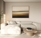 A modern living room features a light beige sectional, a low wooden coffee table with a black bowl, the Amber Fields Canvas Art - Horizontal on the wall, and a tall plant by beige curtains. Soft natural light fills the space.