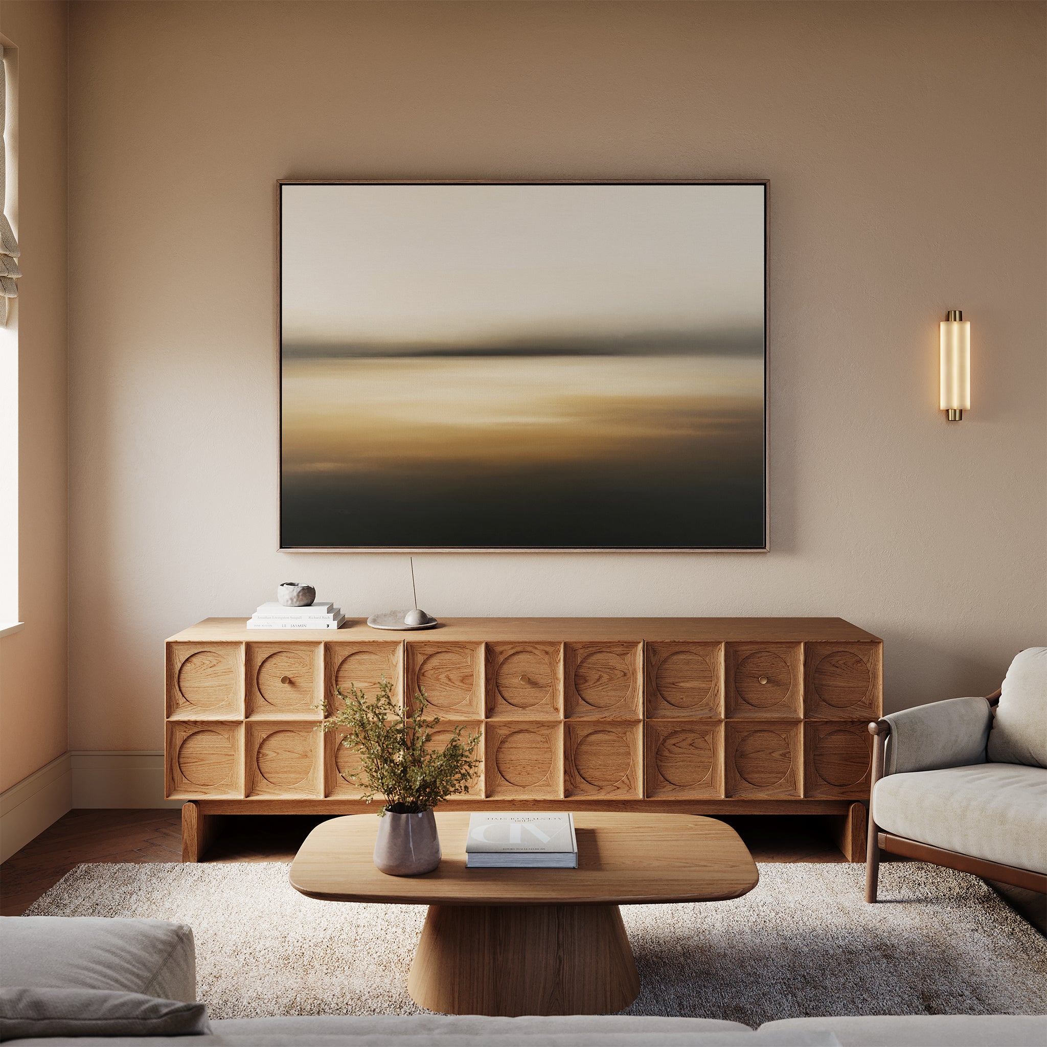 A modern living room with a beige sofa, wooden coffee table, textured sideboard, neutral-toned decor in gentle amber accents, and atmospheric “Amber Fields Canvas Art - Horizontal” wall art featuring an abstract landscape.