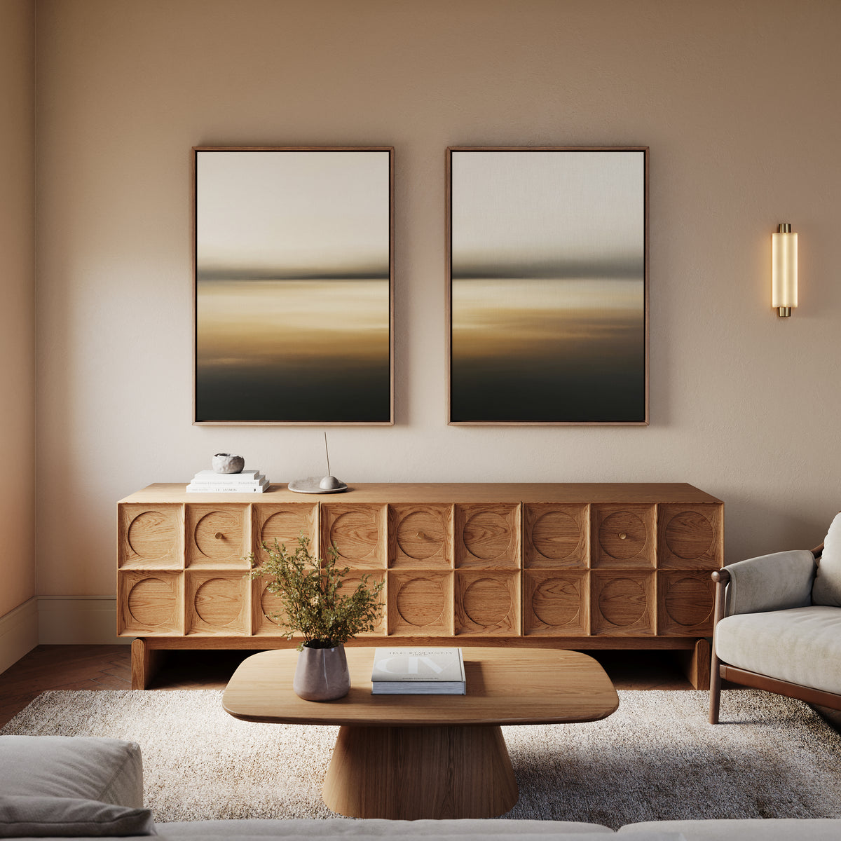 Minimalist living room with light walls, a geometric wooden sideboard, low coffee table, vase with greenery, and Amber Fields - Set Of 2 landscape prints, accented by an elegant wall-mounted light fixture.