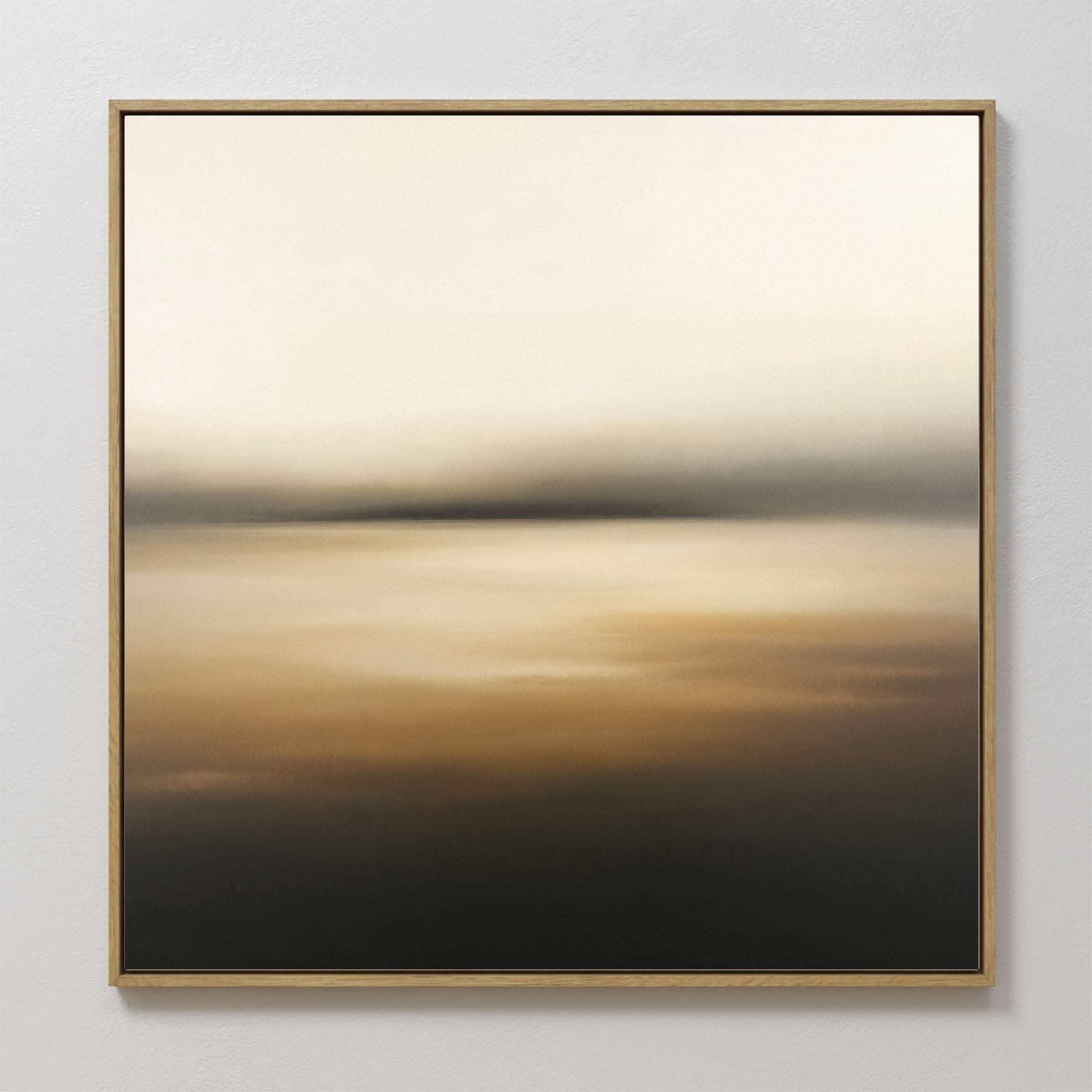 The Amber Fields Canvas Art - Square features soft, blurred gradients of cream, beige, brown, and black with subtle amber accents. This serene landscape print comes in a thin gold frame and is displayed on a white wall.
