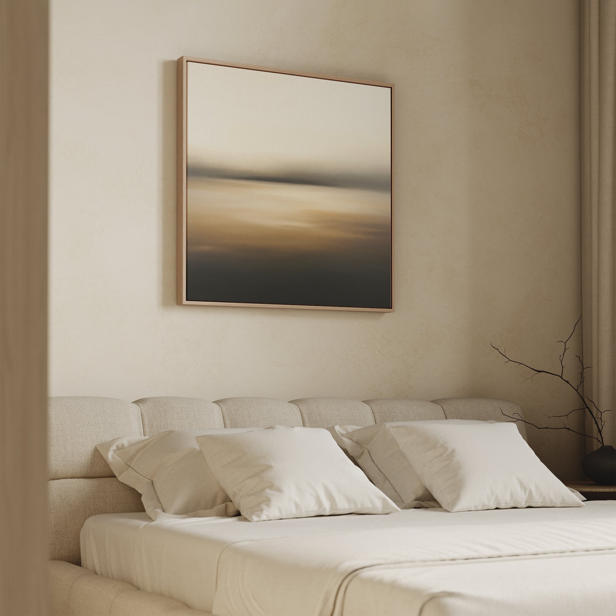 A minimalist bedroom features a beige upholstered bed with white bedding and pillows. Above the headboard hangs the Amber Fields Canvas Art - Square, while a bare branch sits on the bedside table.