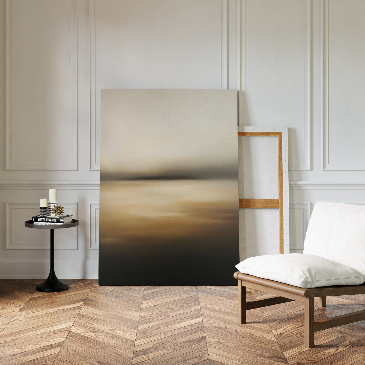 The Amber Fields Canvas Art - Vertical, a large abstract landscape in calming amber tones, leans against a white paneled wall beside a modern chair and small round black side table on a chevron wood floor.