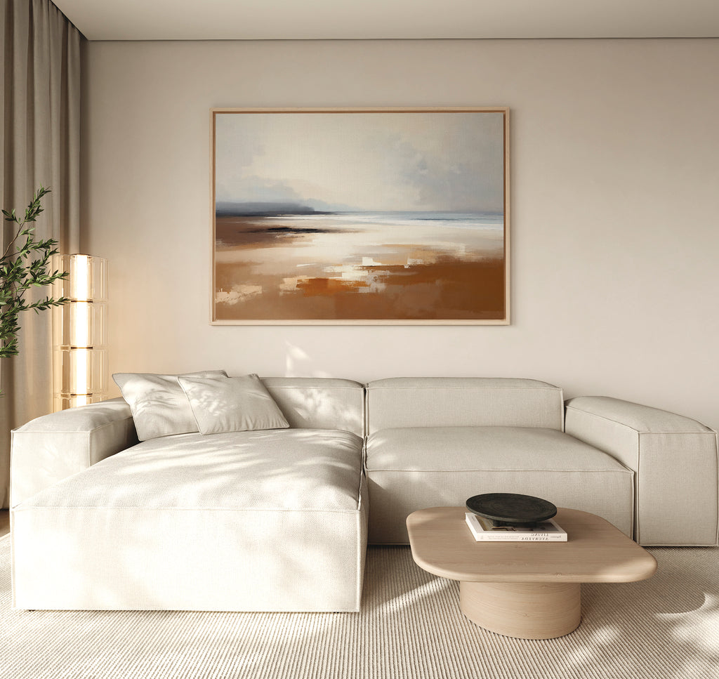 A modern living room with a light beige sectional sofa, wooden coffee table, black decorative bowl, tall plant, and tranquil Amber Shore Canvas Art - Horizontal on a white wall. Natural light fills the space.
