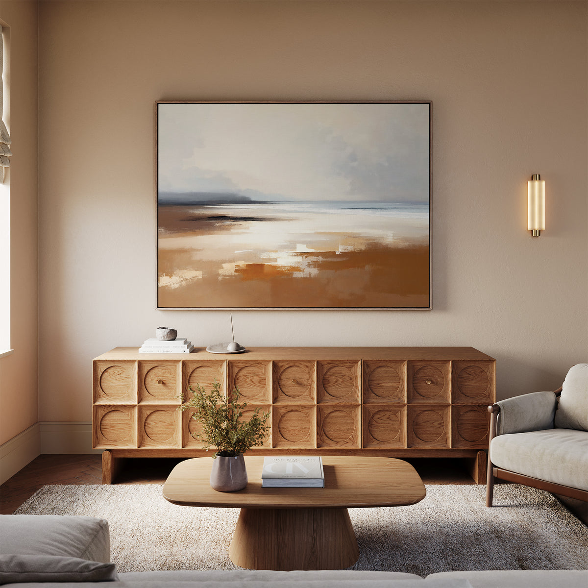 A modern living room features a wooden sideboard, Amber Shore Canvas Art - Horizontal, oval coffee table, light sofa, beige walls, and a vase with greenery. Soft natural light brightens this cozy, minimalist space.