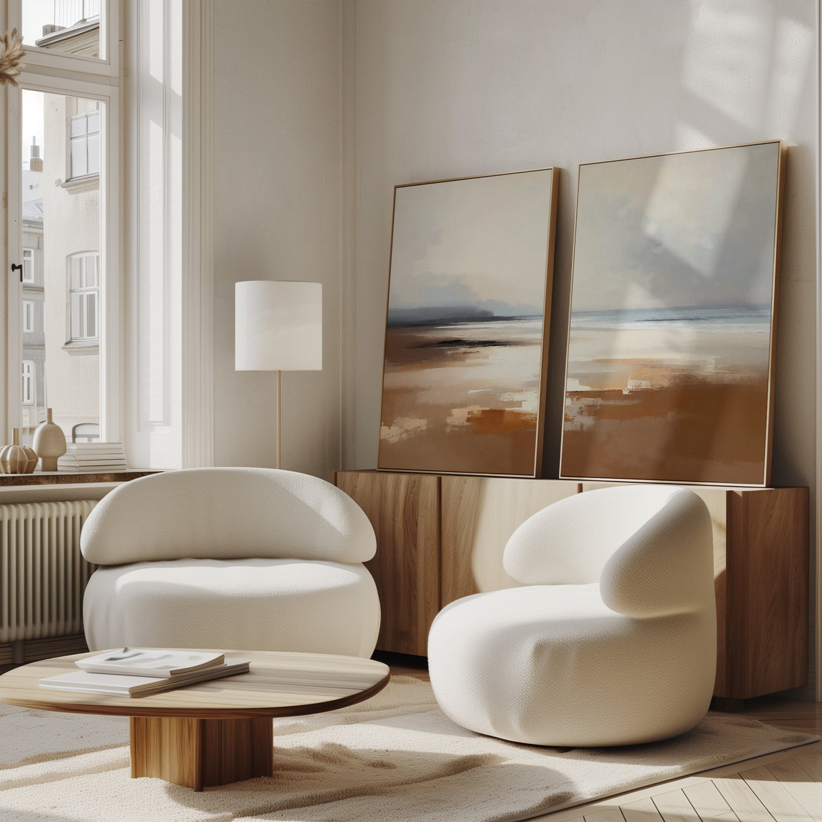 A modern living room with two curved white armchairs, a round wooden coffee table, a floor lamp, and tranquil wall art—Amber Shore - Set Of 2 abstract landscape paintings displayed on a wooden sideboard beneath a large window.