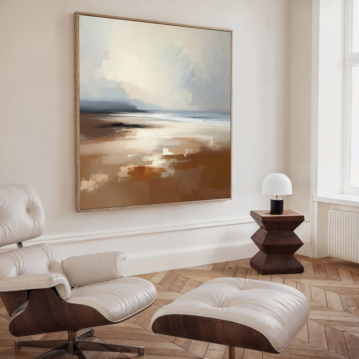 A modern living space with a white lounge chair and ottoman, a geometric wooden side table with lamp, tranquil herringbone wood floors, and Amber Shore Canvas Art - Square hanging on the wall above.