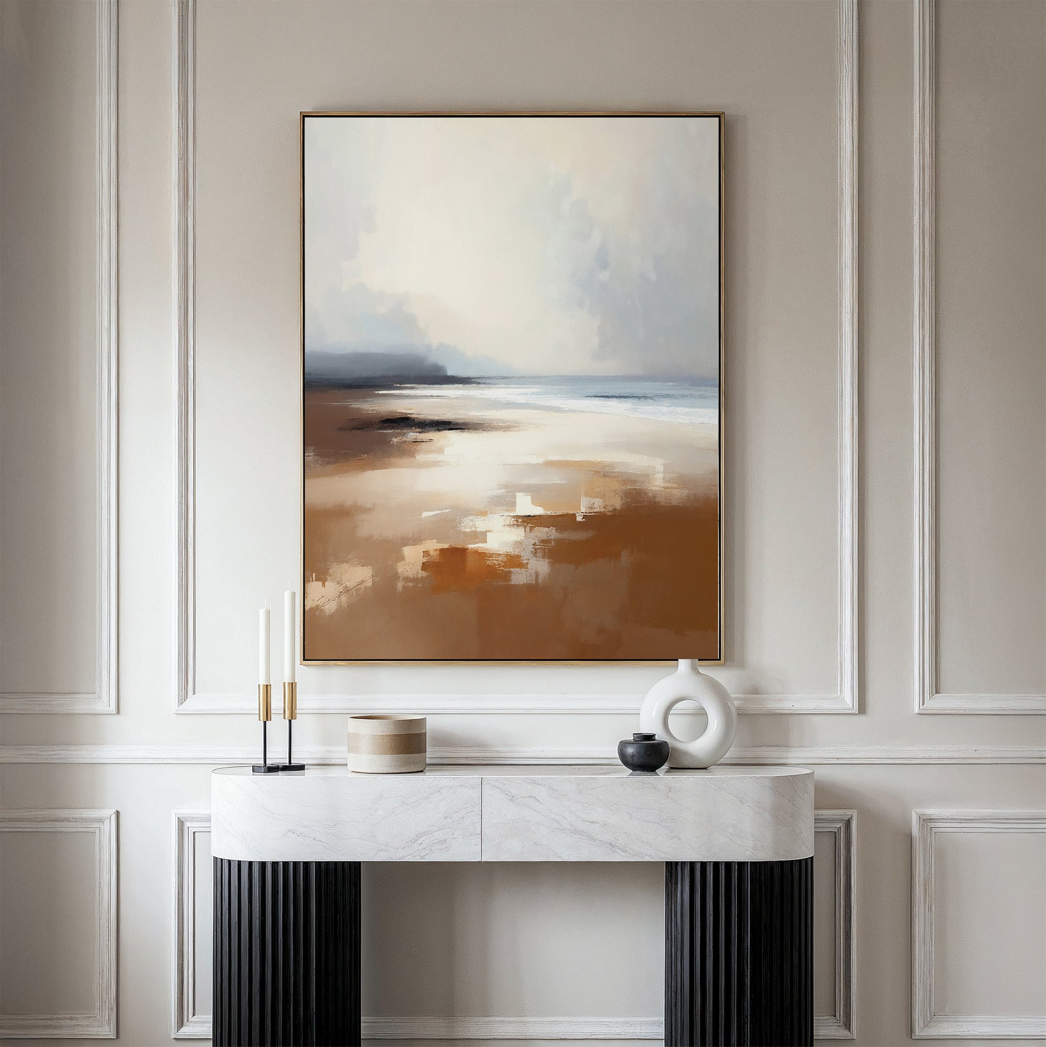 A modern console table with decorative accents stands against a paneled wall, topped by the Amber Shore Canvas Art - Vertical, featuring a tranquil abstract landscape in soft, earthy tones reminiscent of a serene beach scene.