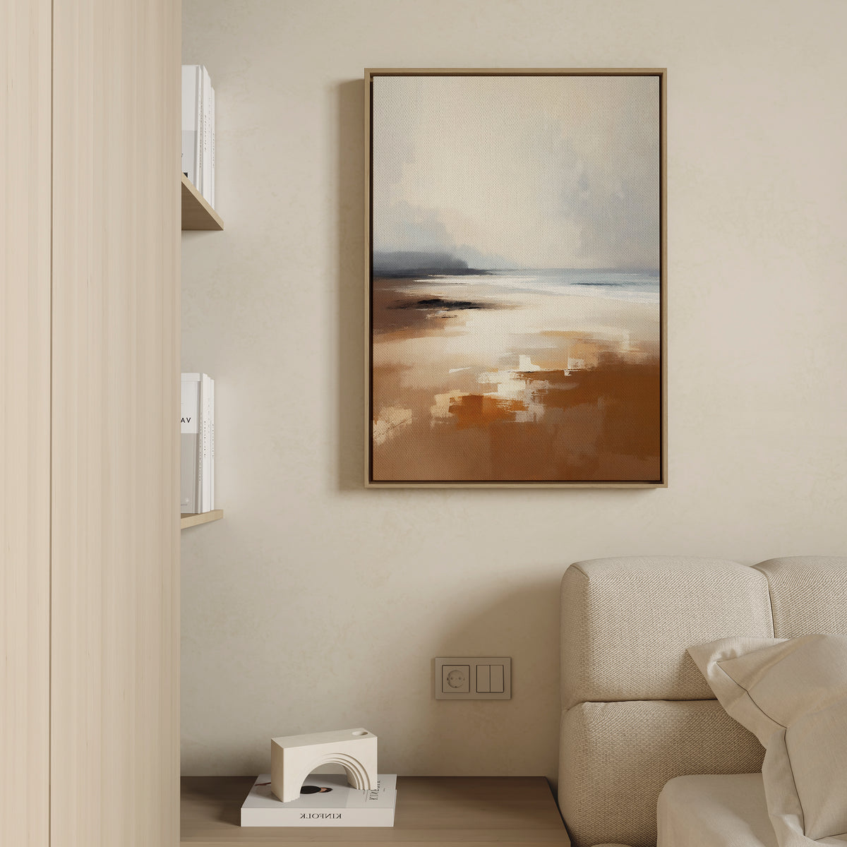 A modern living room with a beige couch, the Amber Shore Canvas Art - Vertical featuring earthy tones above, and a small shelf holding books and a geometric white decorative object.