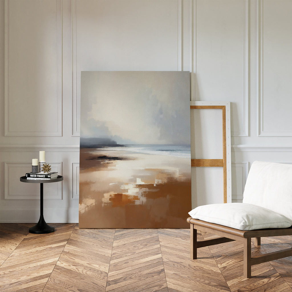 A modern, minimalist room with white paneled walls, herringbone wood floor, the Amber Shore Canvas Art - Vertical resting on the floor, an empty frame, a white cushioned chair, and a small black side table with candles and a book.