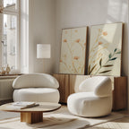 A bright, modern living room features two rounded white chairs, a low wooden coffee table, a floor lamp, and the Autumn Botanicals - Set of 2 canvas prints displayed on a wooden sideboard near large windows.