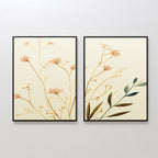 The Autumn Botanicals - Set of 2 features framed canvas prints with minimalist designs—light brown flowers and green leaves on cream backgrounds—adding botanical elegance when displayed together on a white wall.