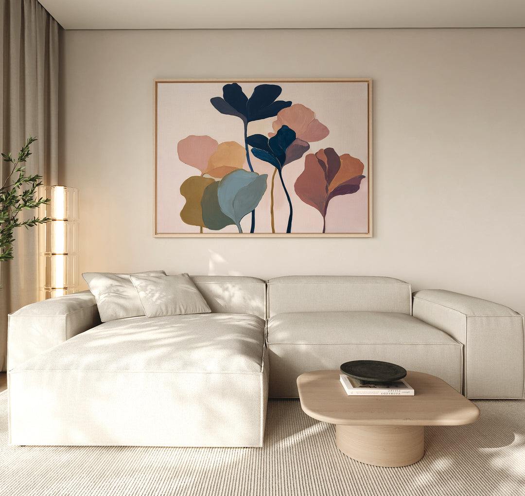 A modern living room features a beige sectional, a light wood coffee table, and the Autumn Garden Canvas Art - Horizontal in pastel tones on the wall. Natural light enters through a window with beige curtains.