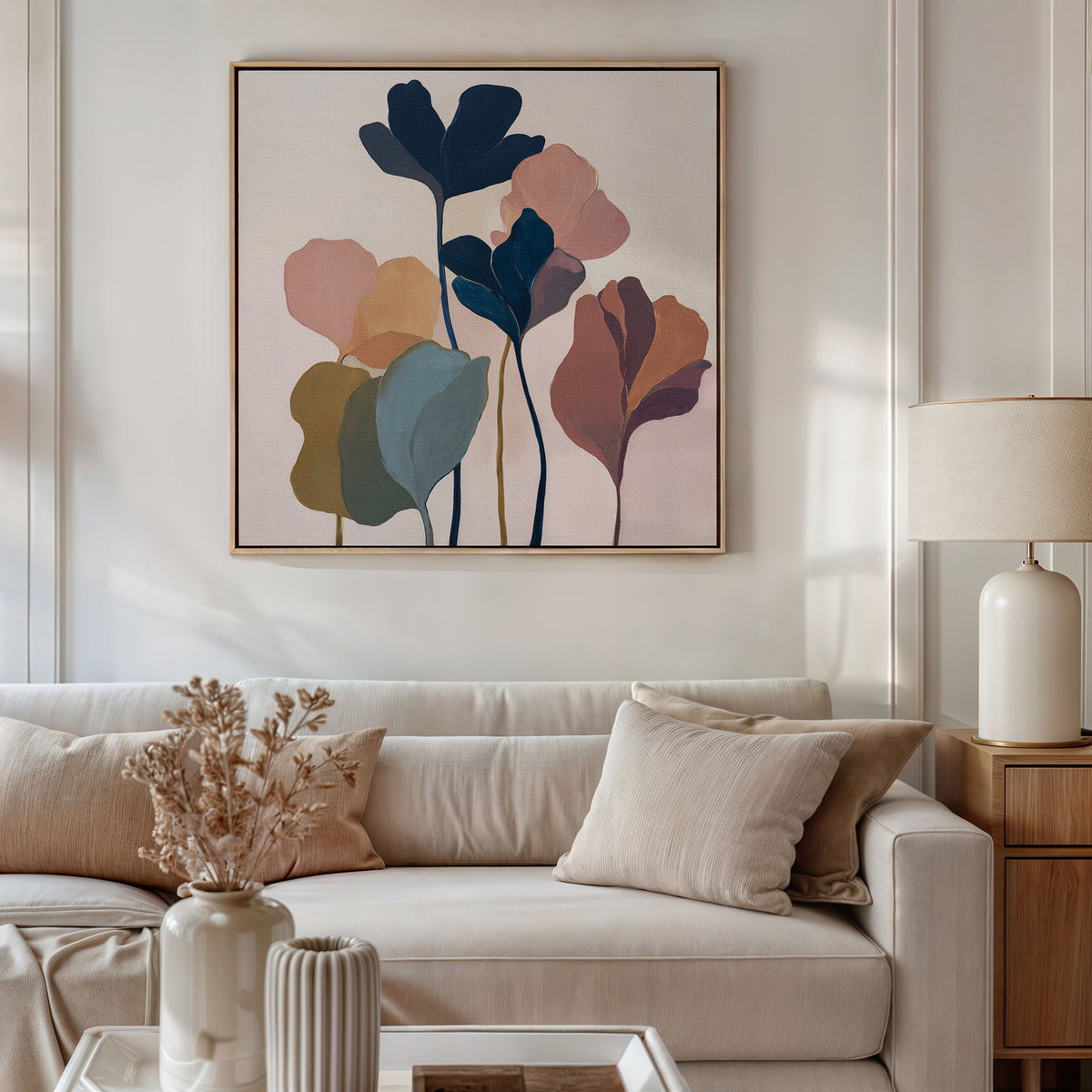 A modern living room with a beige sofa, neutral pillows, and a ceramic lamp on the side table features the Autumn Garden Canvas Art - Square on the wall. A vase of dried flowers adds warmth atop the coffee table.
