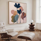 A modern living room features a white lounge chair with ottoman, wooden side table and white lamp, plus the Autumn Garden Canvas Art - Square as botanical wall art. Light wood herringbone floors and neutral walls complete the look.