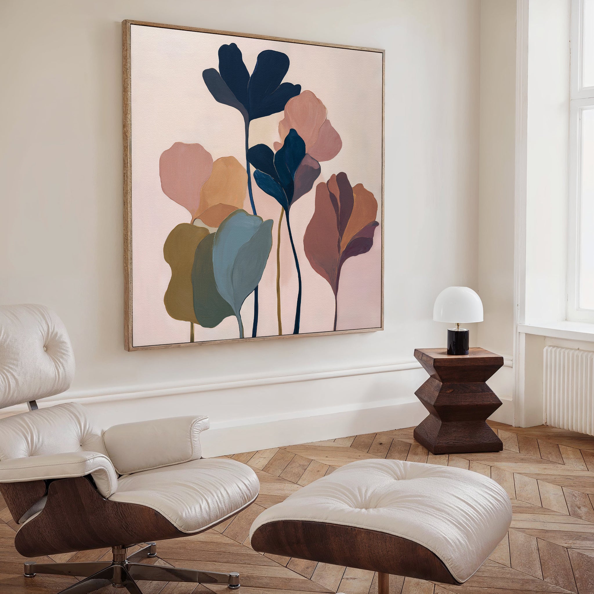 A modern living room features a white lounge chair with ottoman, wooden side table and white lamp, plus the Autumn Garden Canvas Art - Square as botanical wall art. Light wood herringbone floors and neutral walls complete the look.