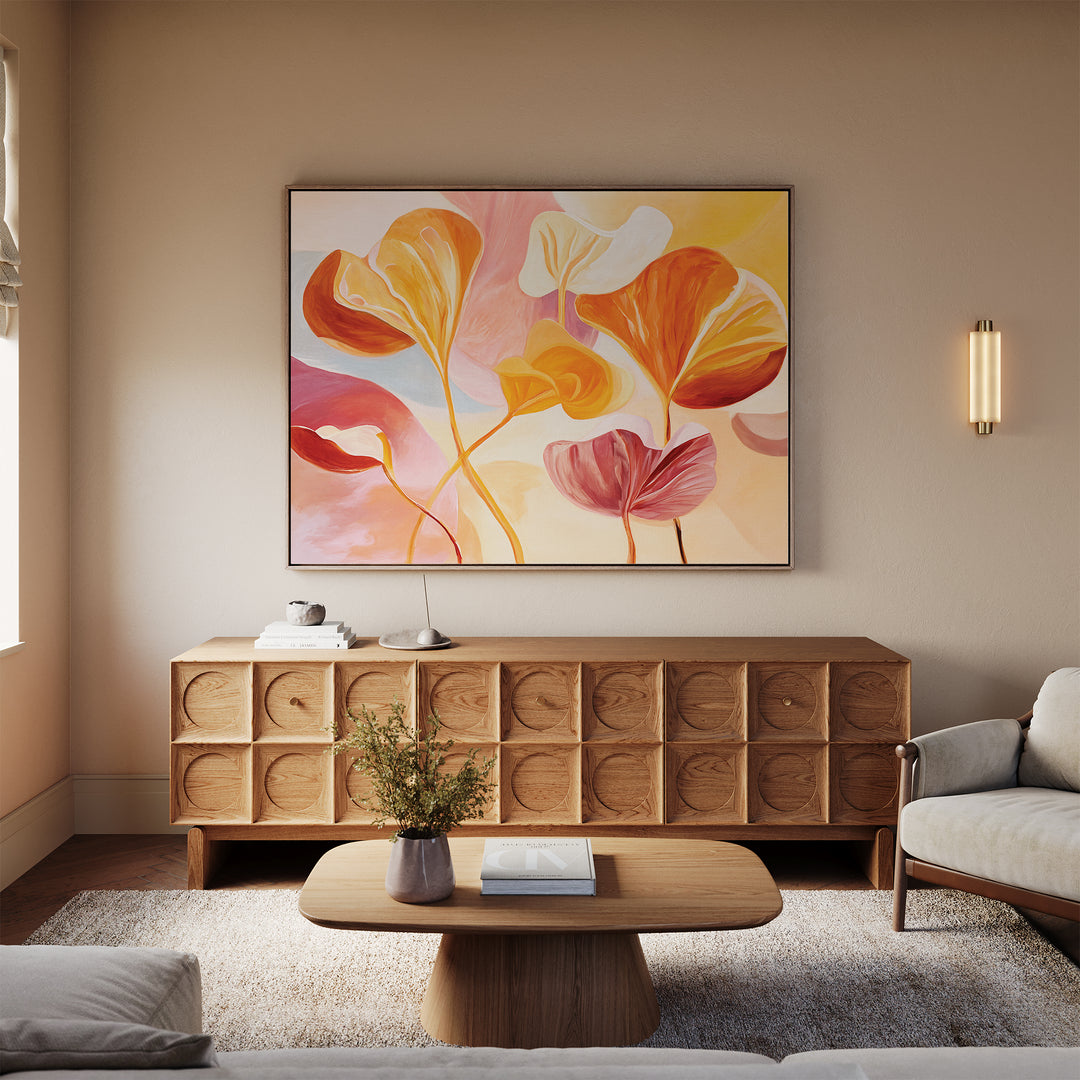 A cozy living room with a light wood sideboard, matching coffee table, beige rug, vase of flowers, and the Autumn Reverie Canvas Art - Horizontal in vibrant orange, pink, and yellow tones brings a Nordic Park vibe to the space.